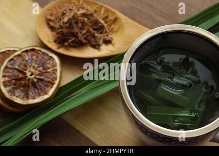 Goiânia, Goias, Brasile – 11 febbraio 2022: Una tazza di tè, con foglie di citronella, alcune fette di arancia disidratata, un cucchiaio con erbe. Foto Stock