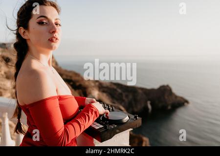 Le mani femminili del DJ suonano la musica mescolando e graffiando durante la festa serale con sfondo marino e caldo tramonto morbido. Primo piano di una console DJ controllata da Foto Stock