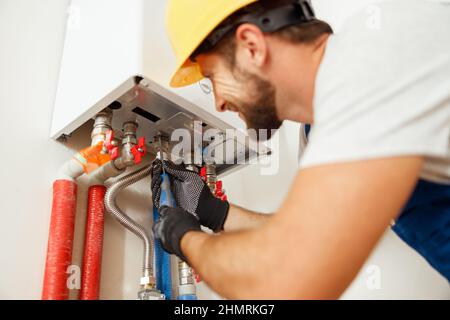 Primo piano dell'idraulico con un cacciavite mentre si fissa la caldaia o il riscaldatore dell'acqua, lavorando sul sistema di riscaldamento in appartamento Foto Stock