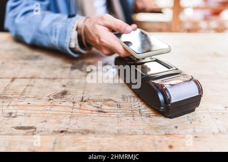 Messa a fuoco morbida di uomo irriconoscibile che tiene il telefono cellulare con chip NFC sul terminale contactless mentre paga l'ordine nel ristorante Foto Stock