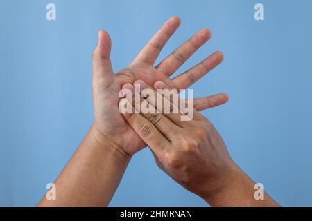 Concetto di sindrome da ufficio. Il palmo delle mani viene massaggiato dopo aver lavorato con le dita. Primo piano isolato su sfondo blu. Foto Stock