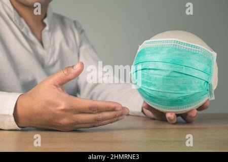 Assicurazione sanitaria in concetto COVID. Un uomo tiene una palla bianca con maschera medica verde. Foto Stock
