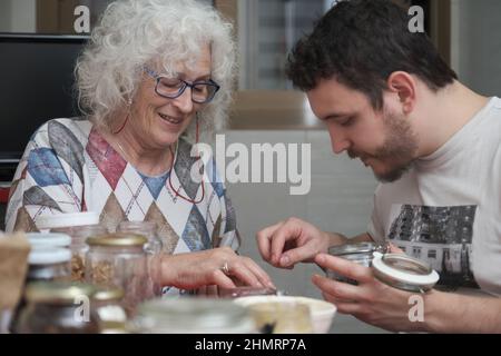 Madre e figlio adulto che preparano qualcosa in cucina insieme. Foto Stock