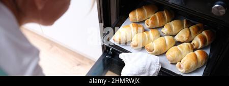 La donna toglie la teglia da forno dei croissant cotti dal primo piano del forno Foto Stock