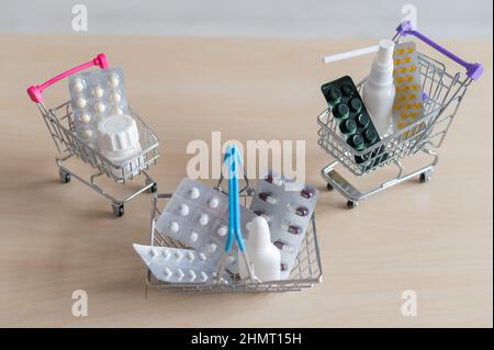 Vista dall'alto su un primo piano di un mazzo di diversi medicinali e carrelli per lo shopping in miniatura. Carrello e cestino pieni di pillole sul tavolo. Concetto di farmacia Foto Stock