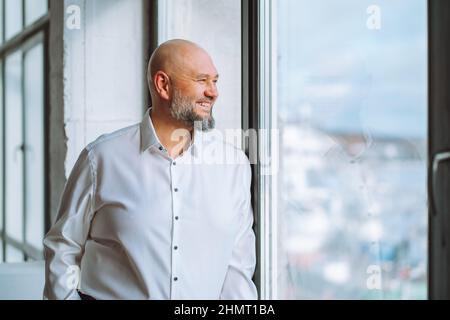 Felice uomo d'affari maturo di successo guardando fuori finestra panoramica in ufficio Foto Stock