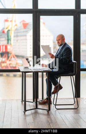 Uomo d'affari maturo alla scrivania d'ufficio che analizza i documenti e fa il lavoro di ufficio Foto Stock