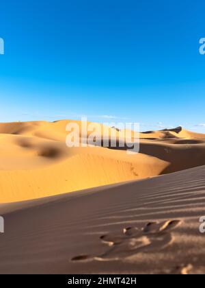 Stampa a mano nella sabbia in primo piano con dune di sabbia di colore giallo dorato e cielo blu nuvoloso sullo sfondo. Foto Stock