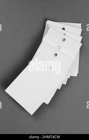 Un mucchio di etichette di cartone di colore bianco per i vestiti con un piccolo foro nella parte superiore di ciascuno posizionato l'uno sull'altro su sfondo grigio scuro. Tag Foto Stock