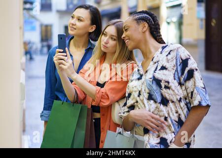 Donne multietniche che scattano foto della vetrina mentre scelgono le merci Foto Stock