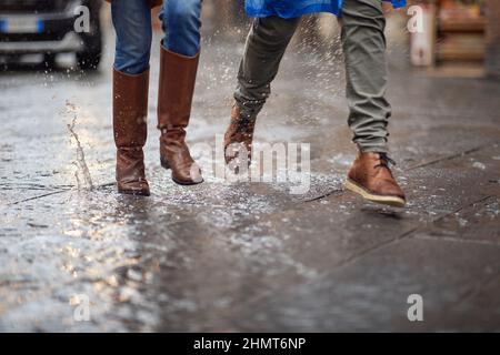 Primo piano di gambe di una giovane coppia che cammina sulla pioggia in città in modo fretta. Passeggiata, pioggia, città, rapporto Foto Stock