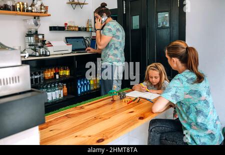 Madre che disegnava con sua figlia mentre il padre lavora nella propria caffetteria. Riconciliazione concetto di vita familiare lavoro Foto Stock