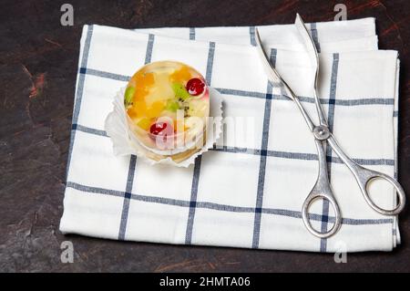 Torta con gelatina, kiwi, ciliegie e mango sul tavolo. Mini dessert yummy su sfondo di legno, primo piano. Foto Stock