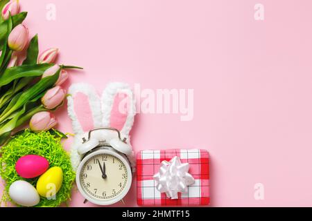 Carta di Pasqua. Sveglia coniglio orecchie dono uova fiori tulipani su uno sfondo rosa. Vista dall'alto dello spazio di copia a disposizione piatta Foto Stock