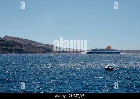 Grande nave da crociera e barca nel mare Egeo preso dalla terra dell'isola di Santorini, Grecia. Trasporto via mare. Barca a vela ancorata in una profonda wate blu Foto Stock