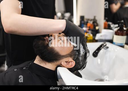 Il parrucchiere lava la testa del cliente in barbiere Foto Stock