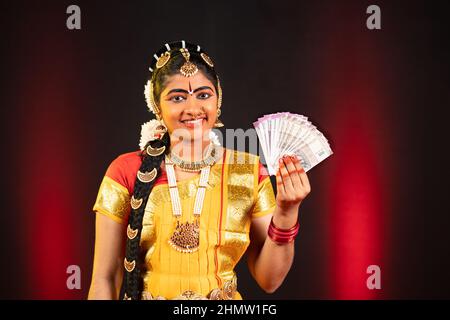 Indiano sorridente Bharatanatyam ballerino che tiene banconote in denaro guardando la macchina fotografica - concetto di guadagni, finanza e banche. Foto Stock