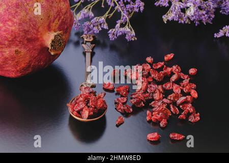 Melograno maturo e anardana secca organica o semi essiccati al sole di frutta melograna su sfondo scuro in cucchiaino di disegno orientale cooper vintage. Foto Stock