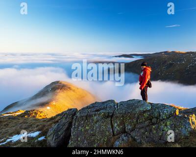 Un alpinista su Red Screes sopra la nebbia di valle da un'inversione di temperatura nel Lake District all'alba, Regno Unito. Foto Stock