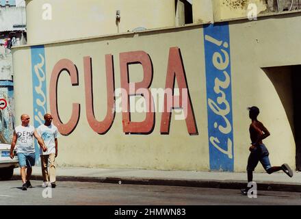 L'uomo scherza pensò l'Avana, via Cuba, mentre gli uomini camminavano verso di lui di fronte ad un murale sulla strada. Foto Stock