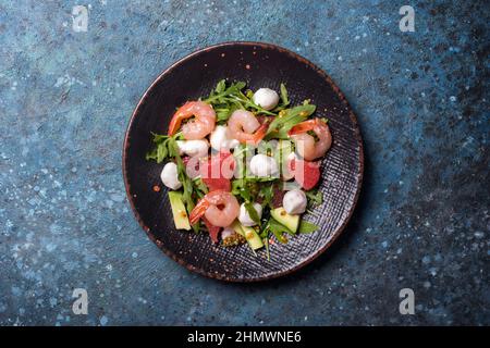 Vista dall'alto di cibi sani e gustosi. Insalata con foglie di rucola fresche, mozzarella, gamberetti, pompelmo, avocado e salsa di senape su cemento blu Foto Stock