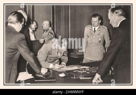 1938, Adolf Hitler firma l'accordo di Monaco di Baviera 30th settembre 1938 "Hitler firma l'accordo di Monaco", sullo sfondo il leader italiano del Facist Mussolini e il capo di Goering della Luftwaffe tedesca in conversazione l'accordo di Monaco è stato concluso a Monaco di Baviera il 30 settembre 1938 dalla Germania, dal Regno Unito, dalla Francia, E l'Italia. Essa ha fornito « la cessione in Germania del territorio tedesco Sudeten » della Cecoslovacchia, Foto Stock