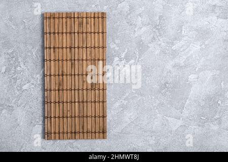 Vista dall'alto del tappeto di bambù per preparare il sushi giapponese su sfondo grigio di cemento con spazio per la copia Foto Stock
