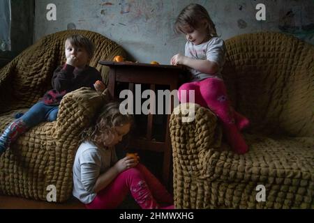 Gornyak, Ucraina. 09th Feb 2022. Andrey, 2, e gemelli Lera e Alyona, 3, mangiano tangerini il 9 febbraio 2022. Igor ed Eugenia, genitori di 5 bambini di età inferiore ai 8 anni, vivono a circa 10 miglia dalle linee di Donetsk a Gornyak, Ucraina. La famiglia lotta per trovare abbastanza lavoro per cibo e bollette e rimane preoccupata quando le forze militari russe si mobilitano sul confine ucraino. (Foto di Michael Nigro/Sipa USA) Credit: Sipa USA/Alamy Live News Foto Stock