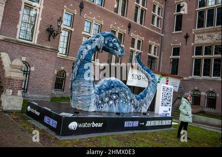 Una donna si vede in posa davanti a Messy, la scultura COP Ness Monster. Durante la celebrazione del COP26 a Glasgow, WaterBear ha collaborato con l'artista Billie Achilleos e jeans CIRCOLARI a marchio denim MUD per creare una scultura del leggendario mostro marino scozzese. A causa della settimana della circolarità olandese, questa scultura costruita in modo sostenibile può essere vista di fronte AL KIT Royal Tropical Institute di Amsterdam per continuare la sua missione di evidenziare la necessità critica di un'economia circolare. Lunga 5 metri e con la pelle di 800 jeans riciclati, Messy è un suggestivo ricordo del mostruoso Foto Stock