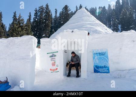 Baramulla, India. 12th Feb 2022. Un lavoratore siede all'ingresso di Igloo Cafè a Gulmarg. Con un'altezza di 37,5 piedi e un diametro di 44,5 piedi, un igloo Cafè, dichiarato il worldís più grande, è venuto alla famosa stazione sciistica di Gulmarg a Jammu e Kashmir, ed è diventato un centro di attrazione per i turisti. Credit: SOPA Images Limited/Alamy Live News Foto Stock
