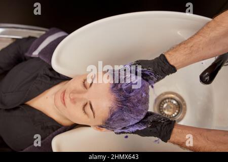 Parrucchiere applicazione di shampoo viola tonificante sui capelli donna Foto Stock