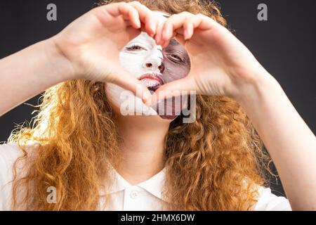 Foto di bella ragazza rossa con volto dipinto in Qatar bandiera facendo segno cuore utilizzando due mani come amore per la sua squadra preferita. Foto Stock