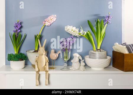 Giacinto bianco in una grande ciotola di porcellana, figurine di lepri e un uccello, sono sul camino contro la parete blu scuro. Layout. Concetto di primavera Foto Stock