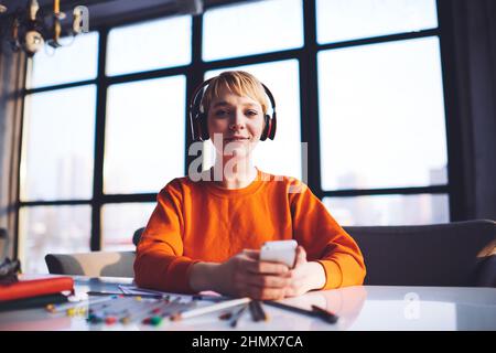 Giovane designer che ascolta la canzone utilizzando lo smartphone lavorando a progetti creativi Foto Stock