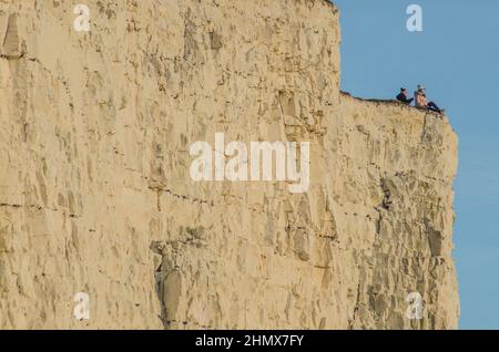 Birling Gap, Eastbourne, East Sussex, Regno Unito. 12th Feb 2022. I turisti rischiano ancora una volta la loro vita posando per le foto sul bordo fragile della scogliera di gesso al punto di bellezza del Sussex. Alcuni sembrano completamente ignari della fragilità, del taglio del gesso & del pericolo estremo che si stanno mettendo dentro. Notare la sottosquadro e la fessura sottostanti. Un incidente in attesa di accadere. Il fotografo era troppo lontano per avvertire qualcuno del pericolo. Credit: David Burr/Alamy Live News Foto Stock