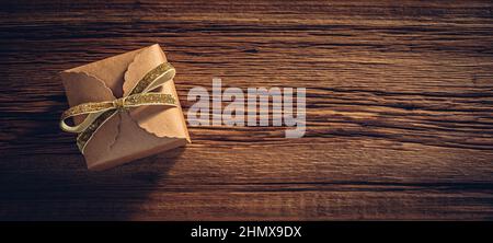 Scatola regalo in carta Kraft con arco in nastro dorato su sfondo di legno Foto Stock
