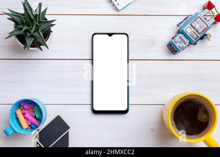 Tavolo da lavoro creativo a disposizione piatta con mockup smartphone circondato da giocattolo robot, tazza di caffè, piante e gesso colorato Foto Stock