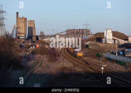 DB Cargo Rail UK classe 66 locomotiva che passa i forni a coke a South Bank (Teeside) con un treno di carri in acciaio vuoti Foto Stock