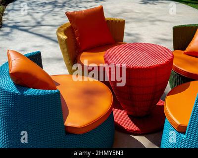 Mobili in rattan colorati e moderni vuoti, tavolo esterno in tessuto con tavolo rotondo e quattro sedie con cuscini sul pavimento in cemento verde. Foto Stock