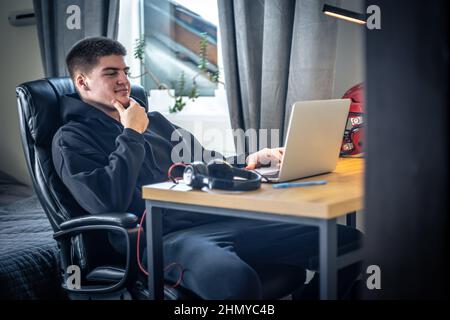 Un giovane atleta maschio si siede di fronte a un computer portatile nella sua stanza. Foto Stock