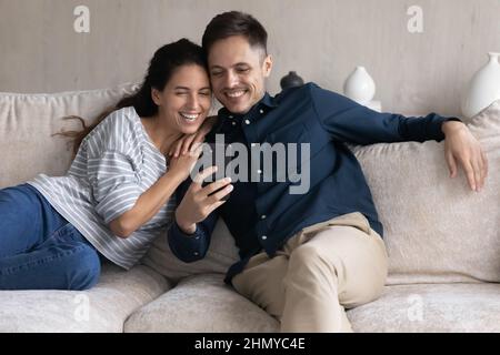 Felice giovane coppia che guarda divertenti contenuti multimediali sullo smartphone Foto Stock