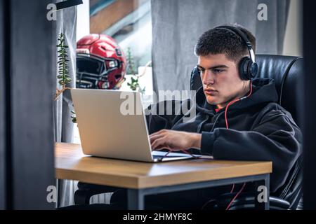 Un giovane atleta maschio si siede di fronte a un computer portatile nella sua stanza. Foto Stock