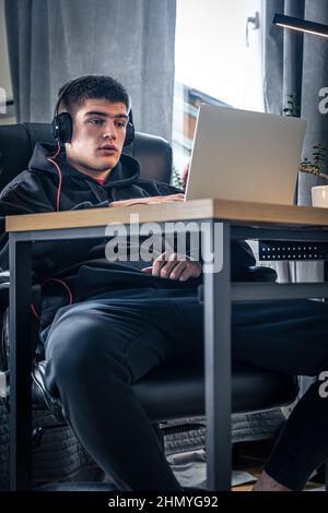 Un giovane atleta maschio si siede di fronte a un computer portatile nella sua stanza. Foto Stock