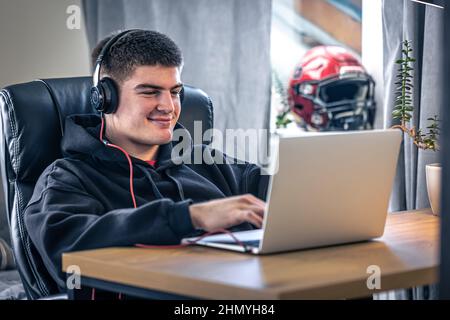 Un giovane atleta maschio si siede di fronte a un computer portatile nella sua stanza. Foto Stock