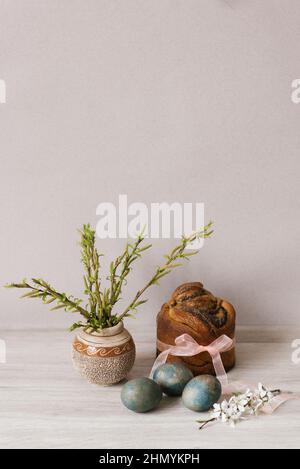 Pasqua o Domenica delle Palme. Uova di pollo dipinte. Uova blu su un tavolo di legno chiaro. Una torta pasquale legata con un nastro di organza. Germogli con germogli sfondo Foto Stock