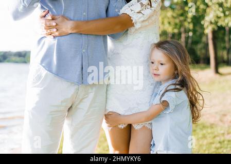 La figlia abbraccia le gambe di sua madre, che abbraccia suo padre. Relazioni familiari e amore Foto Stock