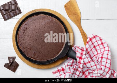 Pancake sottile al cioccolato in una padella su un supporto di legno. Colazione gustosa. Foto Stock