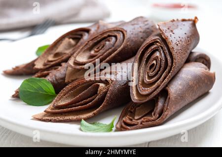 Creme di cioccolato arrotolate disposte in un mucchio e foglie di menta fresca su un piatto bianco. Primo piano. Colazione gustosa Foto Stock