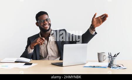 Felice giovane nero imprenditore in abbigliamento formale utilizzando il laptop, gesturing, dimostrare qualcosa, fare presentazione Foto Stock
