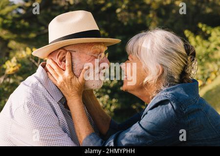 Coppia dai capelli grigi sorridenti l'uno con amore ed affetto. Una coppia felice che condivide un momento romantico mentre si trova in un parco. Allegro eld Foto Stock